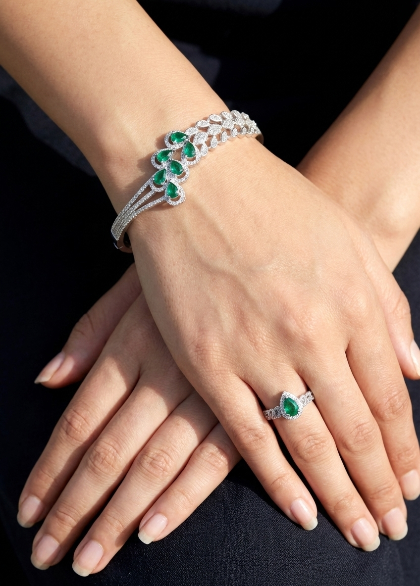 Close-up of hands wearing a bracelet and ring with green gemstones on a dark background