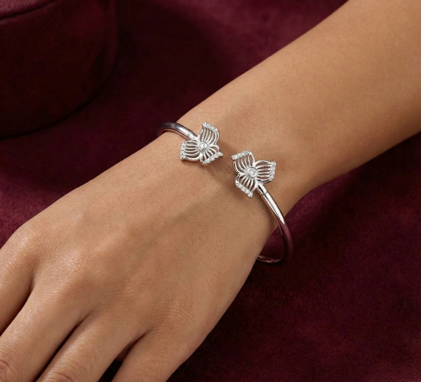 Silver butterfly bracelet on a wrist against a maroon background