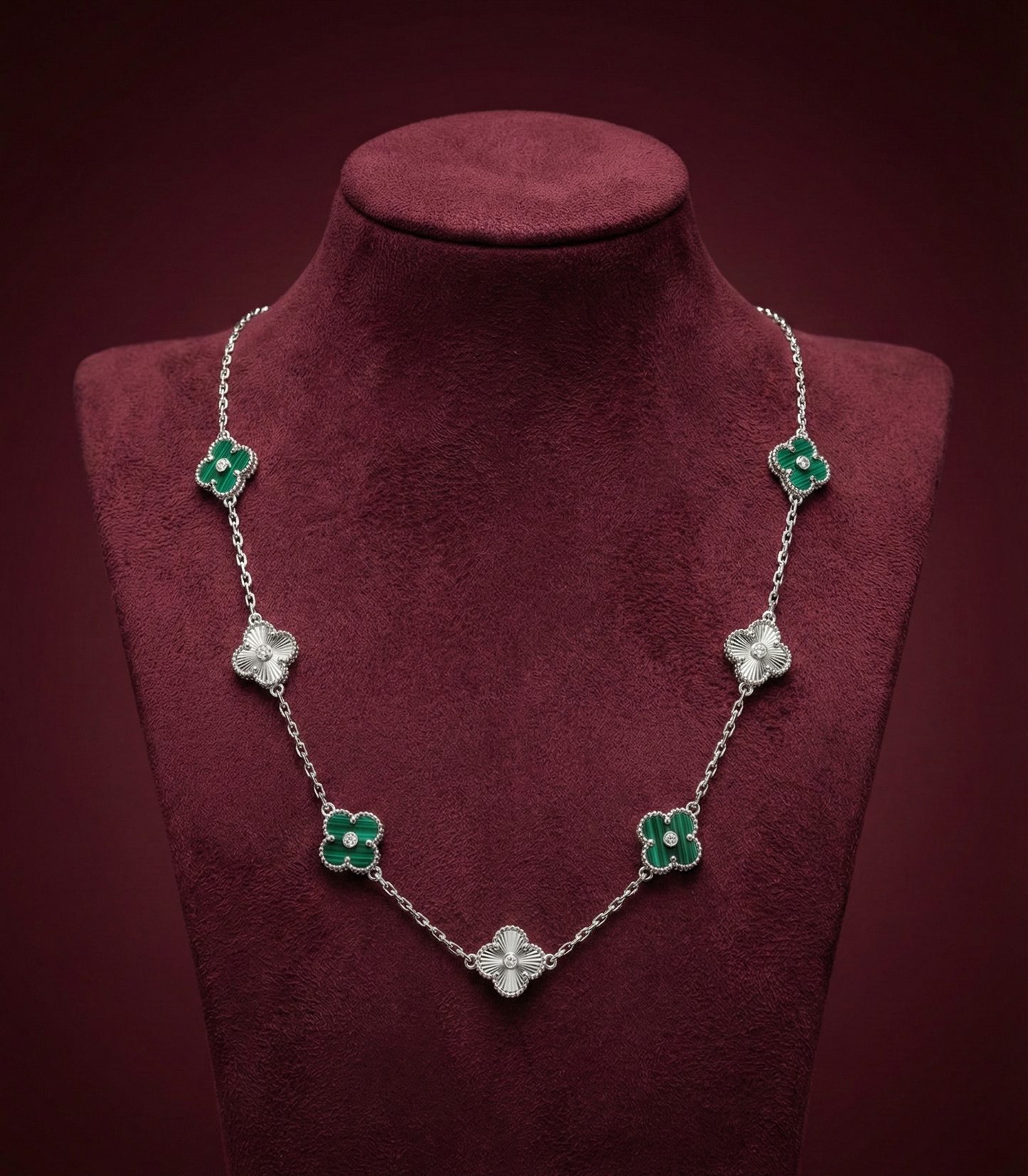 Necklace with green and clear floral pendants on a red velvet stand