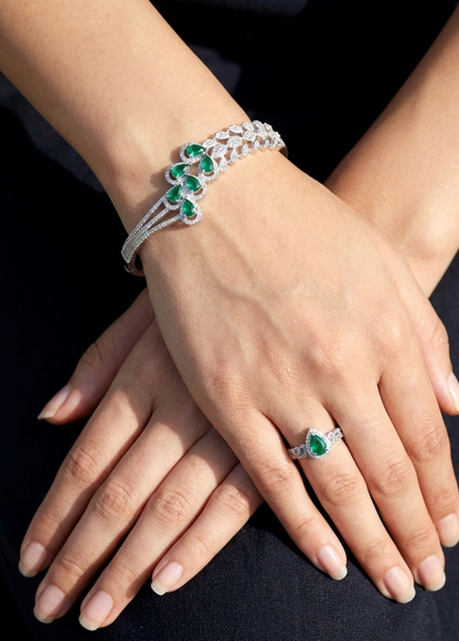 Close-up of hands wearing a bracelet and ring with green gemstones on a dark background