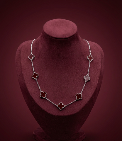 Necklace with clover-shaped pendants on a red velvet stand against a dark red background