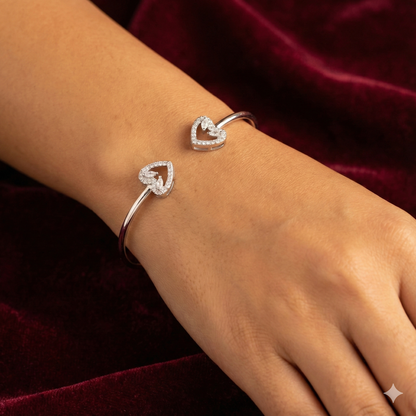 Silver heart-shaped bracelet on a wrist with a red velvet background